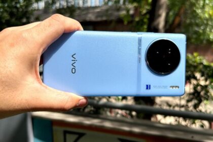 a man hold in in their hand vivo x90 in blue color in greenry background