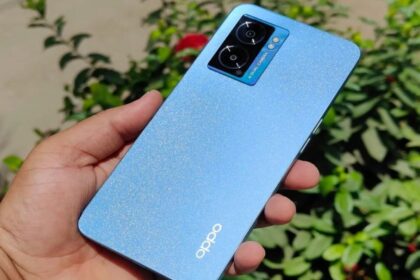 Oppo K10 5G in a hand in blue color infront of green plants