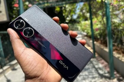 Vivo V29e 5G in dark marron color in hand infront ofsome trees and plants in park