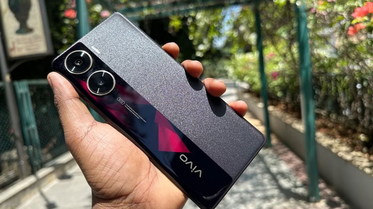 Vivo V29e 5G in dark marron color in hand infront ofsome trees and plants in park