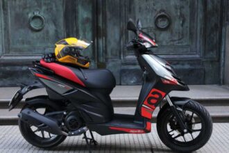 Here is image of Black and red Colour Aprilia SR 160 Scooter Where a helmet is on its seat