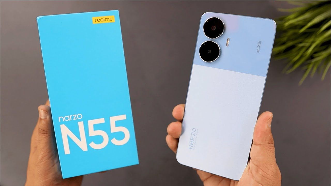 realme narzo n55 in blue color with box in hand infront of grey wall and a plant